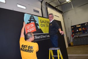 Fire Chief Tom Simkins, on right, hangs a banner at a Community Summit for Galesburg on Track