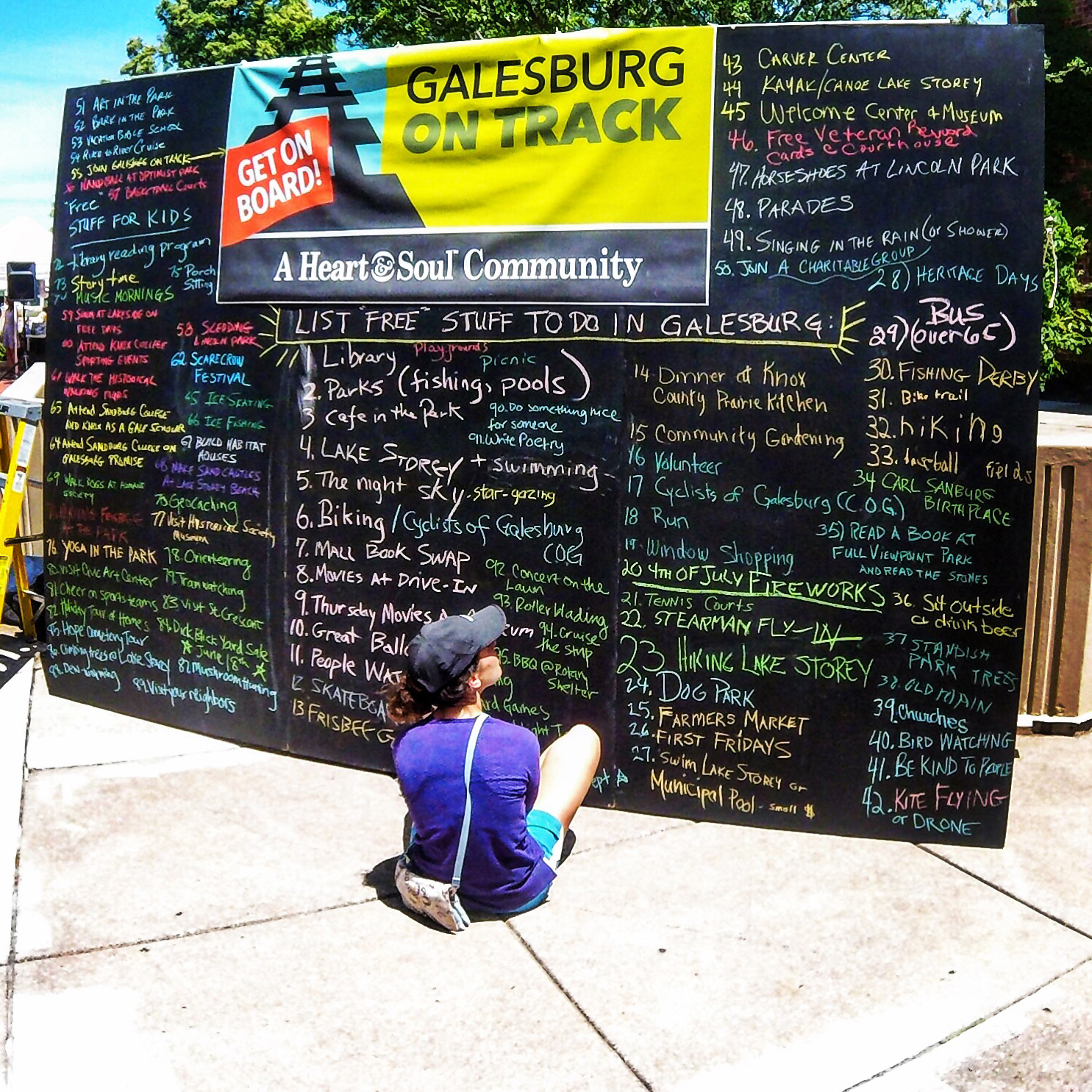 Person sitting in front of large chalkboard that features a list of free things to do in Galesburg, Illinois