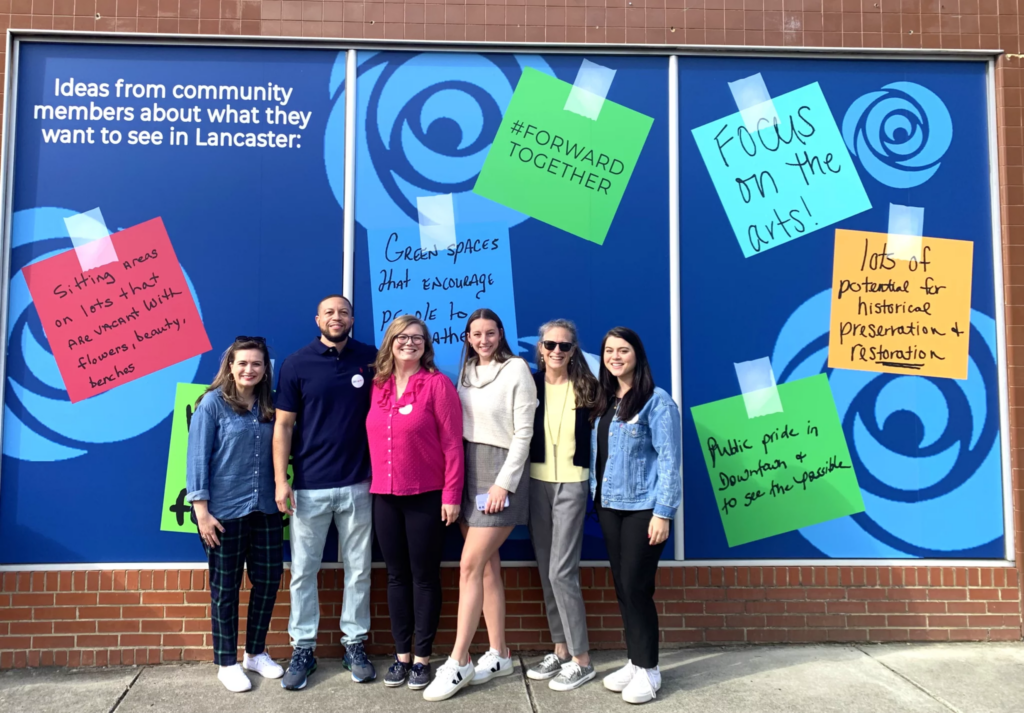 Some of the Arras Foundation staff (from left to right: Elizabeth Howe, Brian Canty, Hannah Saeger Karnei, Emma DeVenny, Susan DeVenny, and Savannah Crosby) pose in front of a mural on historic Main Street in downtown Lancaster, South Carolina. Photo courtesy of the Arras Foundation.