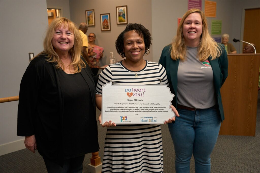 Community Heart & Soul Senior Program Associate Leanne Tingay (left) and PA Humanities Senior Program Officer Jen Danifo, who is a Certified Heart & Soul Coach, help acknowledge and celebrate achievement milestones in the Heart & Soul process in Upper Chichester with Nicole Whitaker, 2nd Ward Commissioner from Upper Chichester, with a PA Heart & Soul plaque. Photo credit: Rustbelt Mayberry Photography.