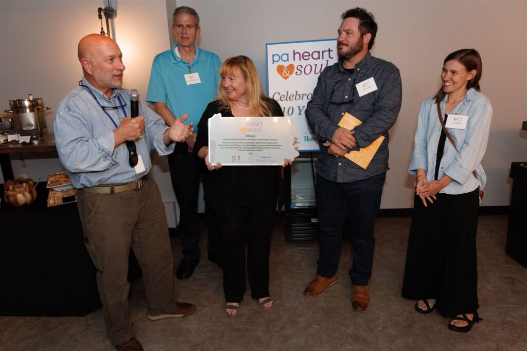 Image of Deputy Secretary Community Affairs and Development Rick Vilello (far left) helps honor the Dillsburg Heart & Soul team on the completion of the process in their town, as Community Heart & Soul Senior Program Associate Leanne Tingay (center) prepares to present the plaque. Dillsburg Heart & Soul team members include Jim Burgess (second from left), Isaac Tucker (fourth from left) and Heidi Tucker (right). Photo by Rustbelt Mayberry Photography.