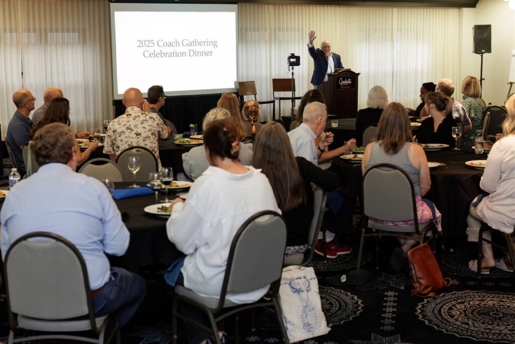 Mark Sherman, President of Community Heart & Soul, standing in front of a crowd of coaches dining together, offering congratulations to all coaches for their collective accomplishments.