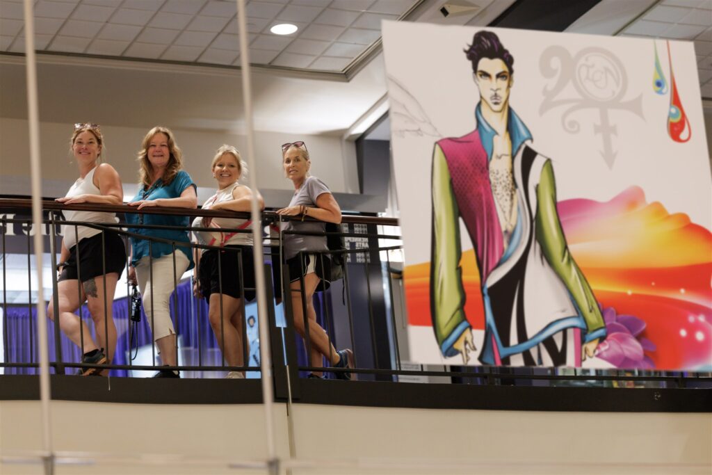 Cat Ingraham, Alice Trowbridge, Maranda Engquist, and Robin Comey visiting Prince: The Tour in downtown Minneapolis, posing with stylized artwork of the aforementioned musician.
